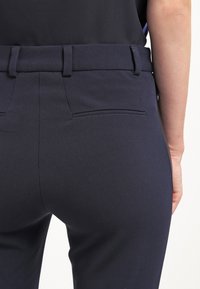 Námořnické kalhoty s přizpůsobeným střihem, hladkou texturou a zadními kapsami; pásek obsahuje poutka pro nastavitelnou velikost.