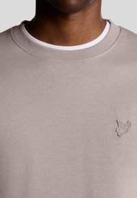 Lichtbeige sweatshirt met een ronde hals en geribbelde mouwen. Voorzien van een klein geborduurd vogellogo op de borst. Smoothed texture.