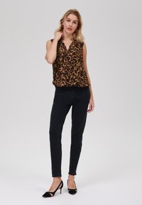 Blusa senza maniche a stampa leopardata marrone abbinata a jeans skinny neri e décolleté a punta neri. Tessuto morbido con un design drappeggiato.