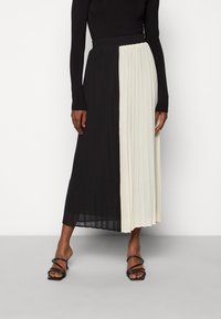 Gonna midi plissettata con un design a blocchi di colore; un lato è nero, l'altro lato è crema. Realizzata in un tessuto leggero con una vita elastica.