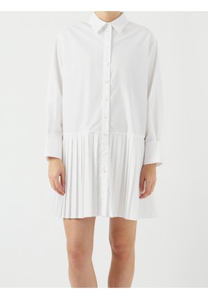 Abito camicia bianco a maniche lunghe con bottoni sul davanti e gonna plissettata indossato da una persona in piedi su sfondo bianco semplice.