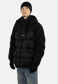 Schwarze Pufferjacke mit durchgehendem Reißverschluss, gerippte schwarze Beanie, passender Schal und Handschuhe, kombiniert mit blauen Jeans. Glatte Textur und gepolstertes Design.