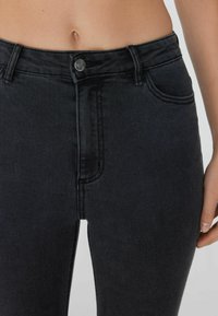 Schwarze Denim-Jeans mit hoher Taille, subtilen Nähdetails, vorderen Taschen und klassischem Knopfverschluss. Glatte Textur, taillierte Passform.