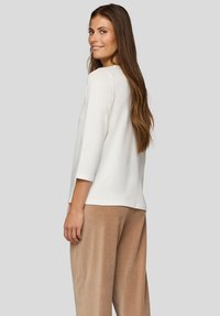 Weißes Langarmshirt mit rundem Ausschnitt. Weiche Textur. Kombiniert mit hellbraunen Cordhosen. Von hinten gezeigt.