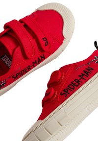 Des chaussures en toile rouges avec deux sangles Velcro, arborant le texte noir "SPIDER-MAN" et des accents graphiques. Semelle en caoutchouc avec une adhérence texturée.