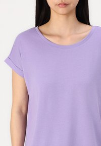 Lilac īsām piedurknēm T-krekls, kas izgatavots no mīksta auduma, ar apaļu kakla izgriezumu un salocītām piedurknēm, ar gludu tekstūru un minimālu dekoratīvo elementu skaitu.