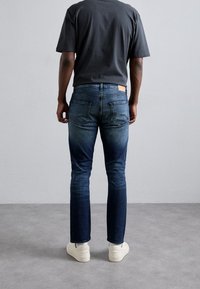 Mörkblå denimjeans med slim fit, med bakfickor, en läderlapp på midjebandet och subtil blekning vid benen.