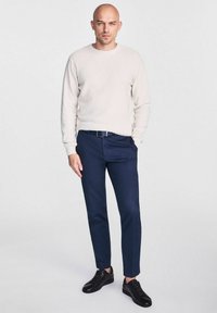 Jasnobeżowy, ribbowany sweter, ciemnonawowe, dopasowane spodnie oraz czarne sneakersy. Prosty design z okrągłym dekoltem i gładką fakturą.