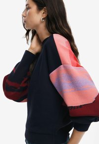 Felpa navy con maniche a maglia sovradimensionate e multicolori in rosa, rosso e viola, con motivi astratti e polsini a coste.
