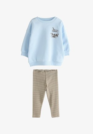 Plavi dukserica s grafikom mliječnog crtića, uparen s prugastim bež i smešnim tajicama. Mekana tkanina, opušteni kroj, rebrasti manžeti.