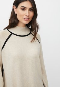 Maglione beige con colletto a coste alto e bordi neri. Texture morbida, vestibilità ampia e maniche raglan. Il design presenta accenti a contrasto.