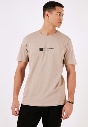 Tricou din bumbac bej cu mâneci scurte, având un text grafic negru și un design pătrat pe față, decolteu rotund și croială standard.