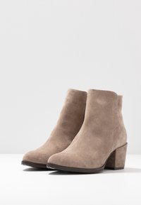 Suède enkelbooties in lichtbruin met een lichtpuntige neus en een gestapelde hak. De textuur is zacht, met strakke lijnen en minimale details.