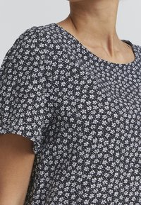 Blusa blu navy con un motivo floreale caratterizzato da piccoli fiori bianchi, maniche corte e scollatura rotonda. Tessuto leggero e strutturato.