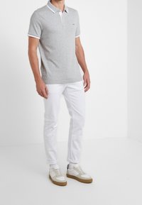 Grå polo med vita detaljer, i kombination med vita byxor och avslappnade sneakers. Skjortan har en klassisk krage och korta ärmar.