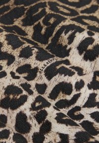 Tkanina s leopardím vzorom na béžovom základe a čiernymi škvrnami, s textúrovaným tkaním. Viditeľný je malý, nenápadný šev.