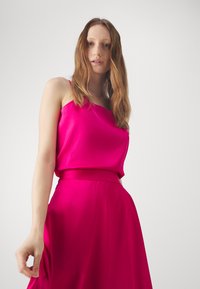 Fuchsia satin top with thin straps, paired with a matching full-length skirt. Smooth texture and a fitted silhouette at the waist.