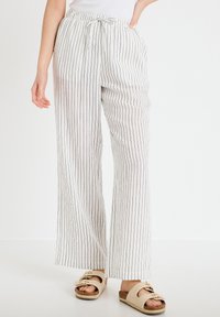 Pantalones blancos de pierna ancha con rayas verticales negras, cintura con cordón, usados con sandalias beige de doble tira sobre un fondo claro y sencillo.