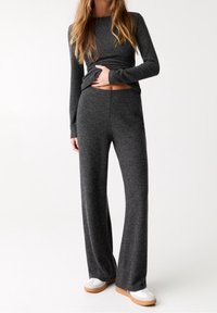 Un haut à manches longues en tricot gris associé à un pantalon large assorti. Le tissu semble doux et texturé ; la tenue a une coupe décontractée. Baskets blanches avec des semelles beiges.