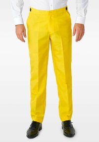 Pantaloni gialli con una texture liscia, frontale piatto e piega lungo le gambe, abbinati a scarpe eleganti nere.