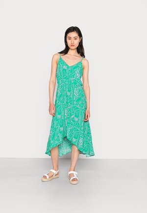 Vestido verde com padrão, alças finas e uma bainha assimétrica. Apresenta um desenho floral em branco, combinado com sandálias brancas.