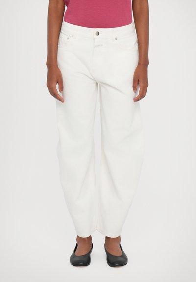 Pantalons en denim blancs, amples et taille haute, avec cinq poches et une fermeture à bouton. Portés avec une chemise rose et des ballerines noires.