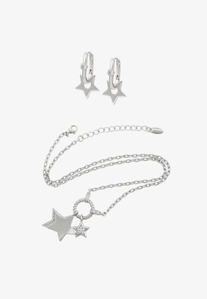 Silberne, sternförmige Ohrringe mit einem kleinen Edelstein. Die Halskette besitzt mehrere Kettenlagen und zwei Sternanhänger, von denen einer mit Steinen verziert ist.
