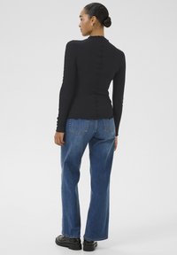 Maglietta nera a maniche lunghe con bordo ondulato, abbinata a jeans azzurri a gamba larga e scarpe con plateau nere.