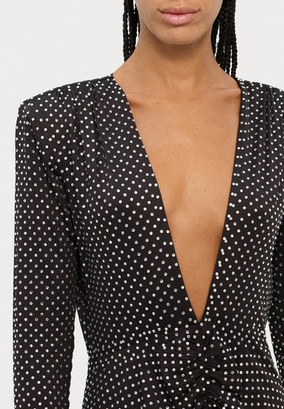 Zwarte jurk met een diepe V-hals, lange mouwen en een gerimpelde taille. Versierd met zilveren embellishment over het geheel.