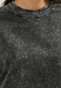 Felpa girocollo di un grigio scuro, trattata con un effetto minerale, presenta un colletto a costine e un tessuto morbido e testurizzato con un motivo sottile in tutta la superficie.