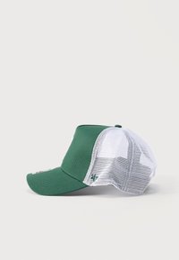 Πράσινο και λευκό καπέλο τύπου trucker με δίχτυ και κυρτή γείσο, εμφανισμένο από το πλάι σε απλό ανοιχτόχρωμο φόντο.