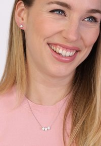 Zilveren sieradenset met studoorbellen met heldere edelstenen en een bijpassende ketting met drie gegroepeerde edelstenen. Het model heeft lang haar.