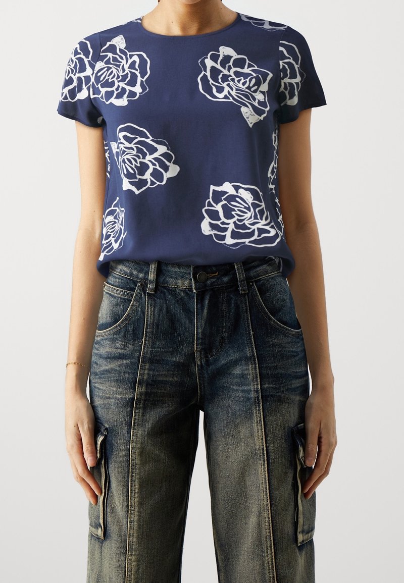 Mörkblå kortärmad topp med stora vita blommönster, tillsammans med urtvättade vida jeans cargo-byxor.