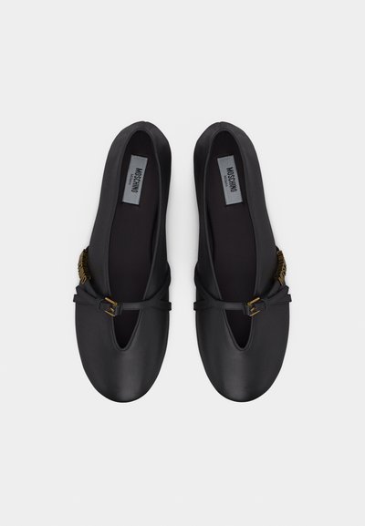 Paire de ballerines en cuir noir avec une petite bride et une boucle dorée, portant l'inscription Moschino Milano à l'intérieur.