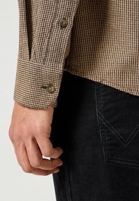 Brązowo-kremowa mankiet koszuli w kratę pepitkę z dwoma guzikami, zestawiona z czarnymi sztruksowymi spodniami z kontrastowym wzorem szwów.