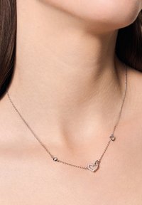 Srebrny naszyjnik z łańcuszkiem, wyposażony w dużą zawieszkę w kształcie serca oraz mniejszy charms w kształcie serca, ozdobiony małymi, przezroczystymi kamieniami.