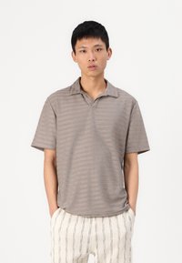 Camisa polo cinza às riscas de mangas curtas com colarinho, apresentando um corte descontraído e uma textura suave, combinada com calças claras e estampadas.