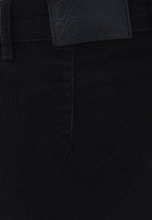 Pantaloni in velluto a coste nero con tessuto strutturato, dettagli cuciti e una toppa in pelle con marchio a rilievo in vita.