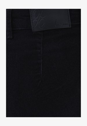 Pantalones de pana negros con tejido texturizado, detalles cosidos y una parche de cuero con marca en relieve en la cintura.