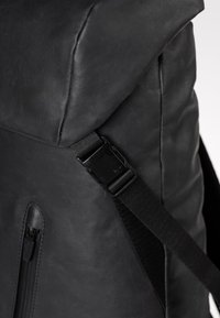 Schwarzer Leder-Rucksack mit strukturiertem Design, glatter Textur, verstellbarem Riemen und einer Reißverschlusstasche an der Seite.
