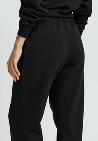 Sorte sweatpants lavet af blødt stof, med en tapered ben-design, elastisk talje og synlige sidelommer. Glat tekstur.
