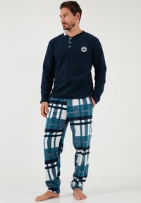 Marineblaue Fleece-langärmelige Oberteil mit drei Knöpfen und Logo, kombiniert mit blau-weißen karrierten Flanell-Hosen, die eine Mischung aus Streifen aufweisen.