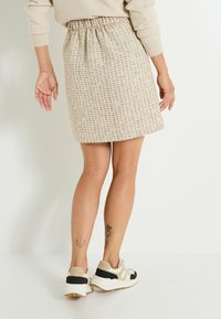 Falda de punto en beige claro con tejido texturizado, cinturilla elástica y largo hasta medio muslo; combinada con zapatillas deportivas que presentan acentos en marrón y negro.