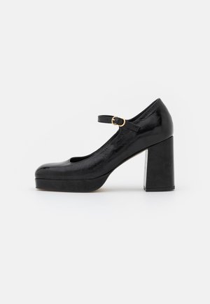 Chaussure Mary Jane en cuir verni noir avec bout arrondi, talon haut épais, semelle plateforme, et bride de cheville ajustable avec une boucle dorée.