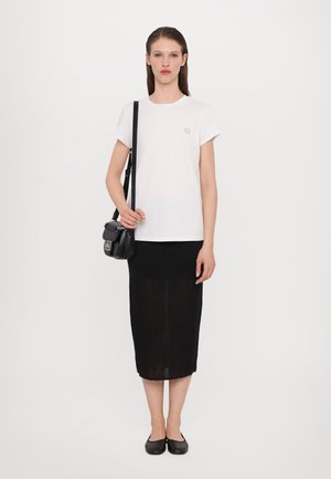 Camiseta de algodón blanca con mangas cortas y un pequeño logo, combinada con una falda midi negra texturizada y un bolso cruzado negro. Bailarinas negras sencillas.