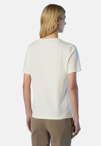Camiseta de algodón crema con mangas cortas y cuello redondo, que presenta una textura suave y un corte relajado. Costuras visibles en el dobladillo.