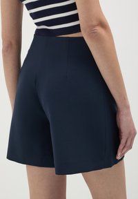 Donna che indossa pantaloni corti a vita alta di colore blu navy e un top corto a strisce blu e bianche, mostrata di spalle.