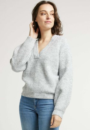 Pull en tricot gris clair avec un col en V et une texture côtelée. Présente des manches longues légèrement bouffantes et une coupe décontractée.
