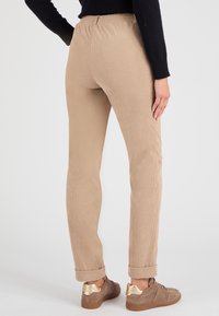 Beige corduroy broek met een getailleerde pasvorm, elastische tailleband en opgerolde boorden. Draagt bij lichtbruine sneakers met gouden accenten.
