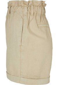 Short beige taille haute avec ceinture élastique, passants pour ceinture, poches fendues latérales et ourlet roulé, présenté de profil.